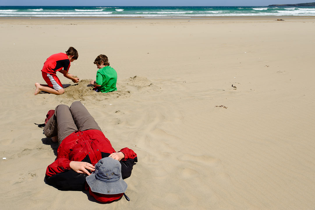 Anne napping, protected from hard, wind-blown, sand; Southland; South Island; New Zealand